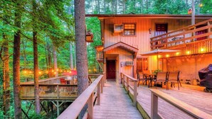 A wooden cabin with a deck, surrounded by trees.