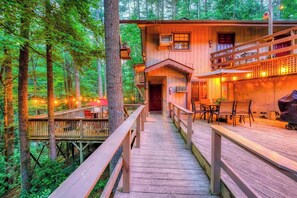 A wooden cabin with a deck, surrounded by trees.