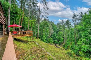 A wooden deck with a red umbrella, overlooking a forested area with a stream.