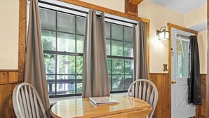 A wooden dining table with two chairs, a book on the table, and a door with a coat hanging on it. - The Cascades Inn (Tiger)