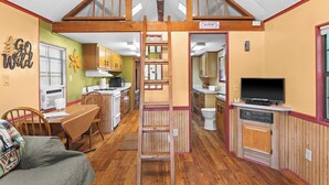 A compact kitchen with wooden cabinets, a dining area with a table and chairs, and a lofted sleeping area with a ladder. - The Cascades Inn (Tiger)