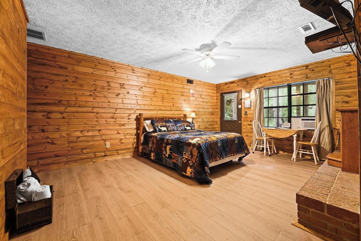 A log cabin room with a bed, a desk, and a window.