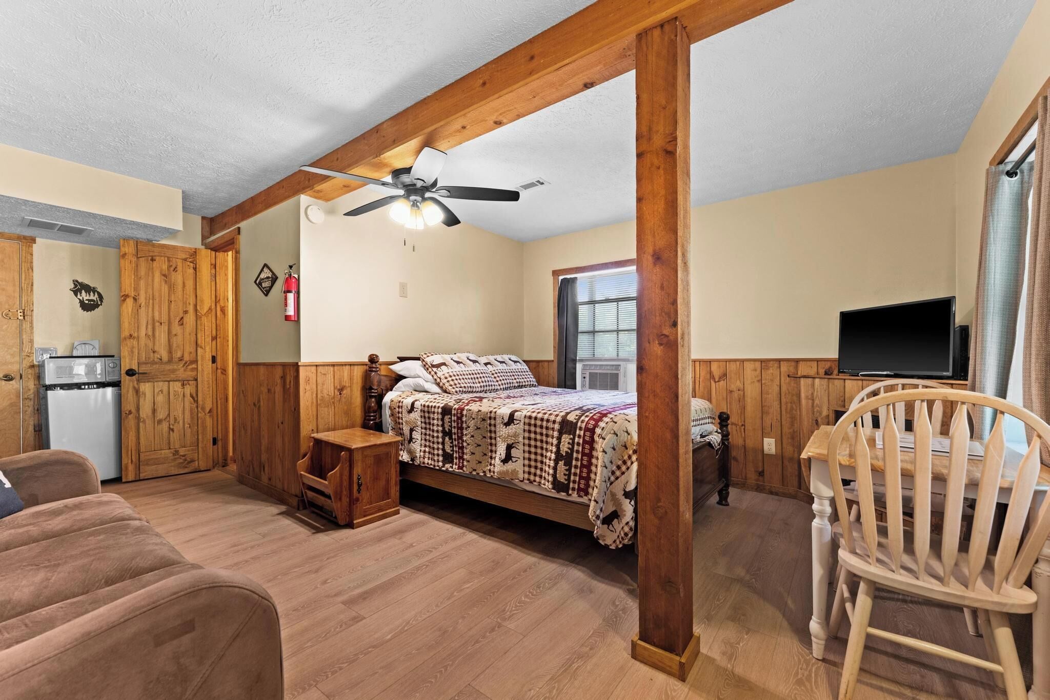 A cozy room with a bed, wooden walls, a ceiling fan, a TV, and a wooden chair.