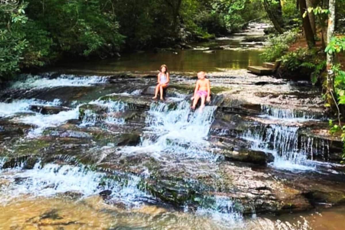 A natural waterfall with two individuals sitting on rocks.