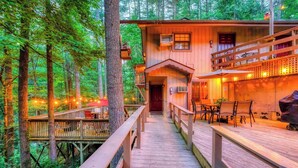 A wooden cabin with a deck, surrounded by trees.