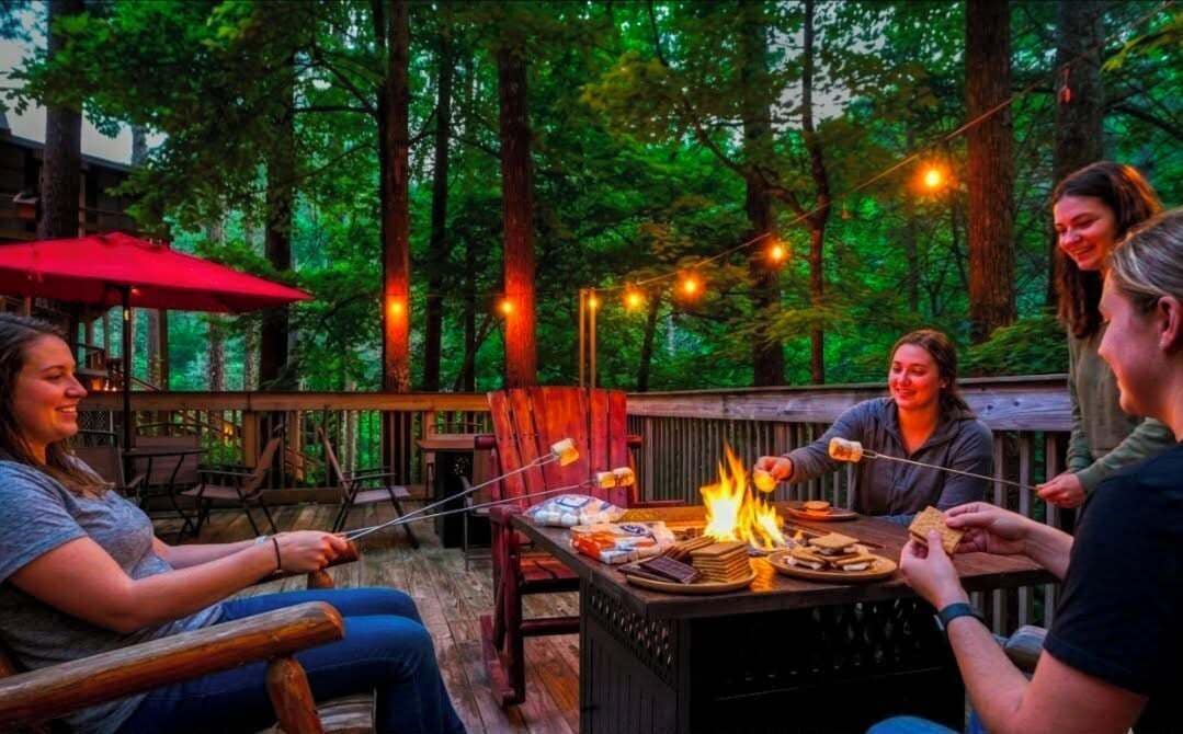 Un espacio exterior para comer con un brasero, terraza de madera y luces colgantes.