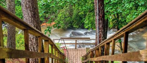 A wooden bridge leading to a waterfall surrounded by dense green foliage.