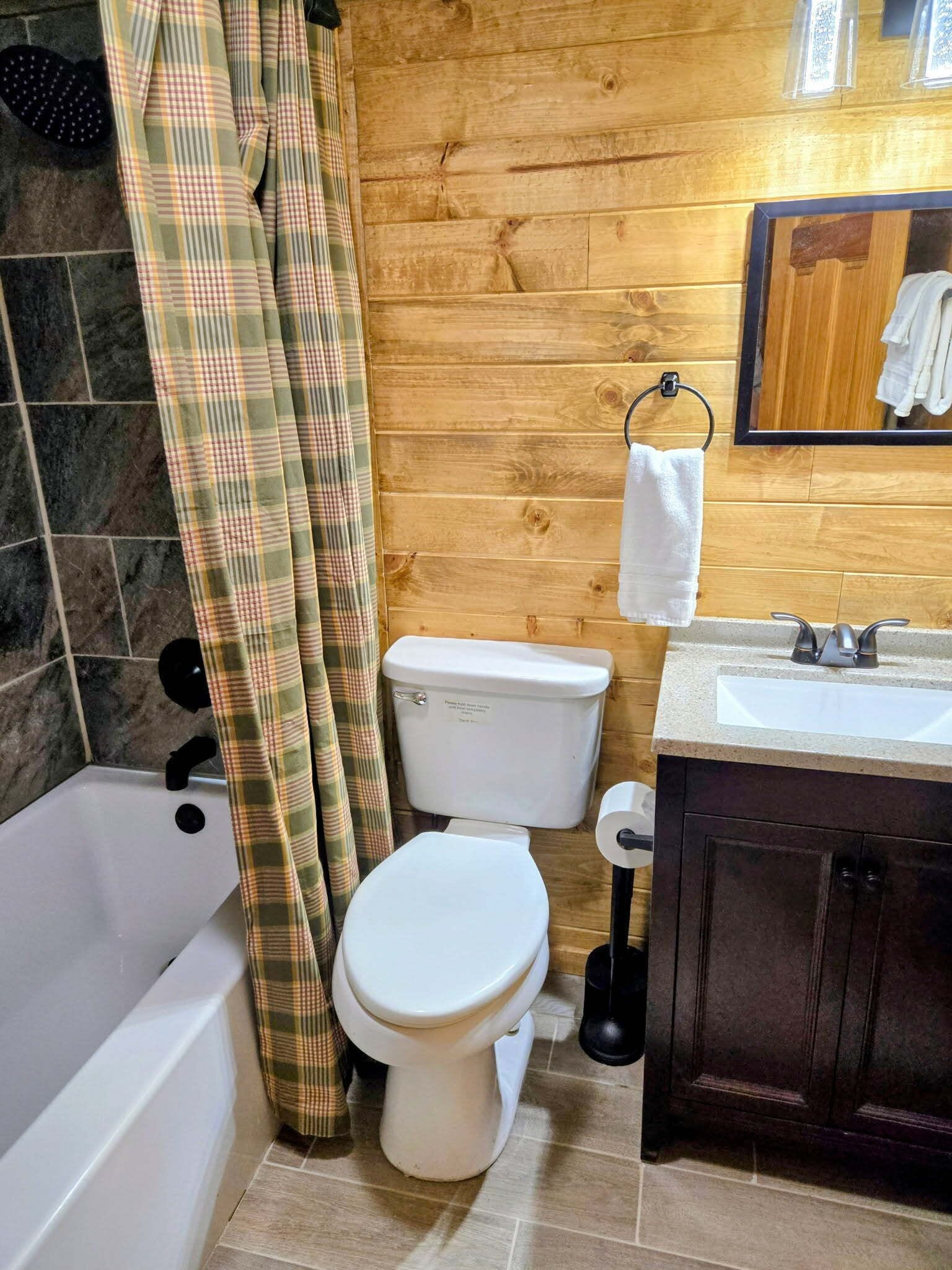 A bathroom with a wooden wall, a white toilet, a bathtub, and a sink with a mirror above it.