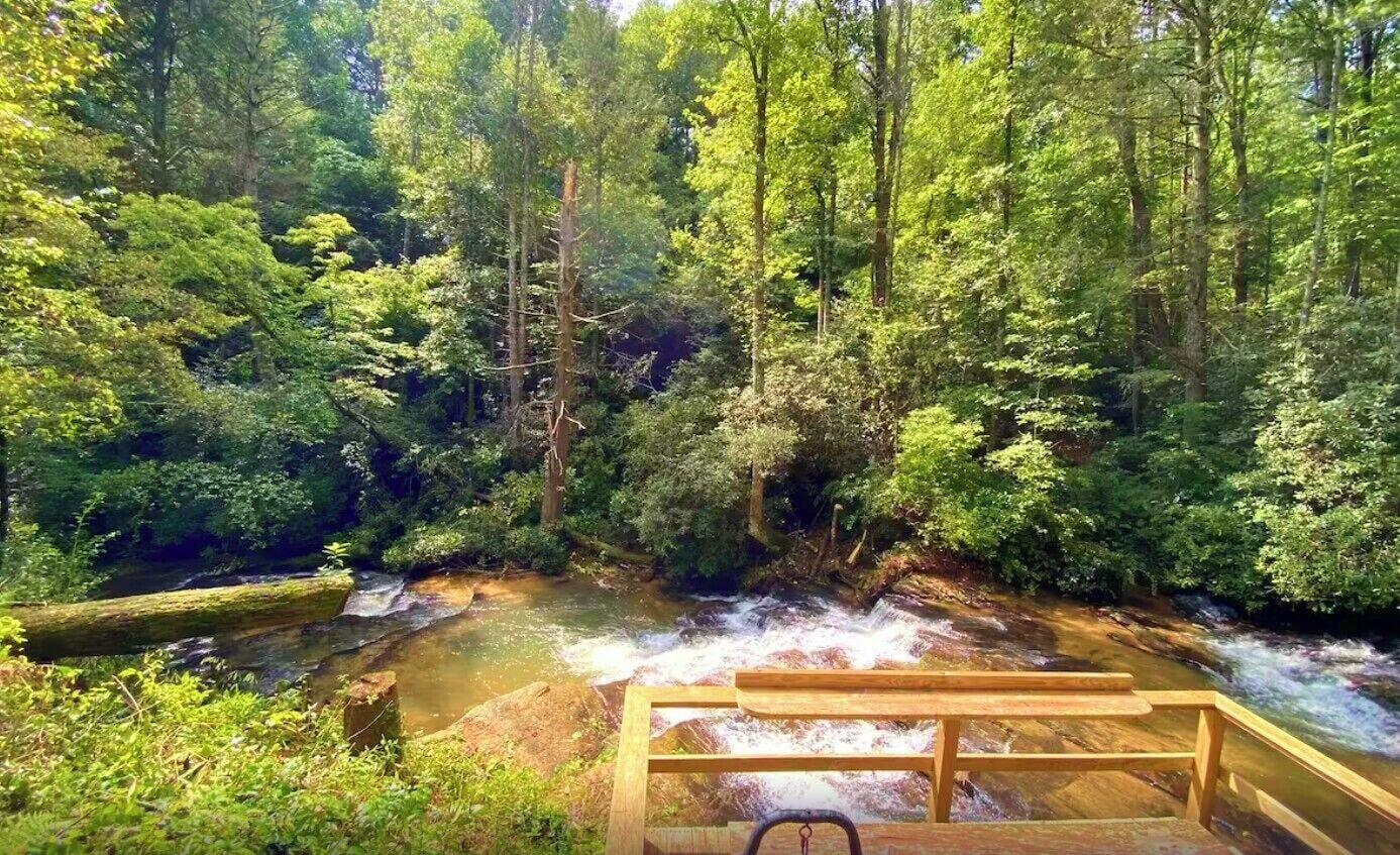 Una terraza de madera con vista a un área boscosa y un arroyo.