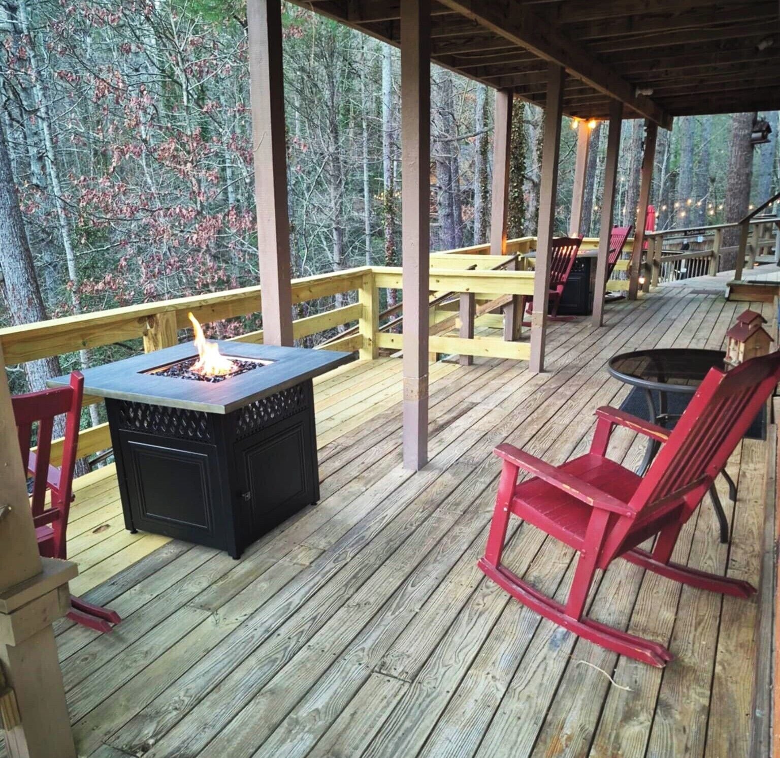 A covered outdoor deck with a fire pit, red chairs, and a table.
