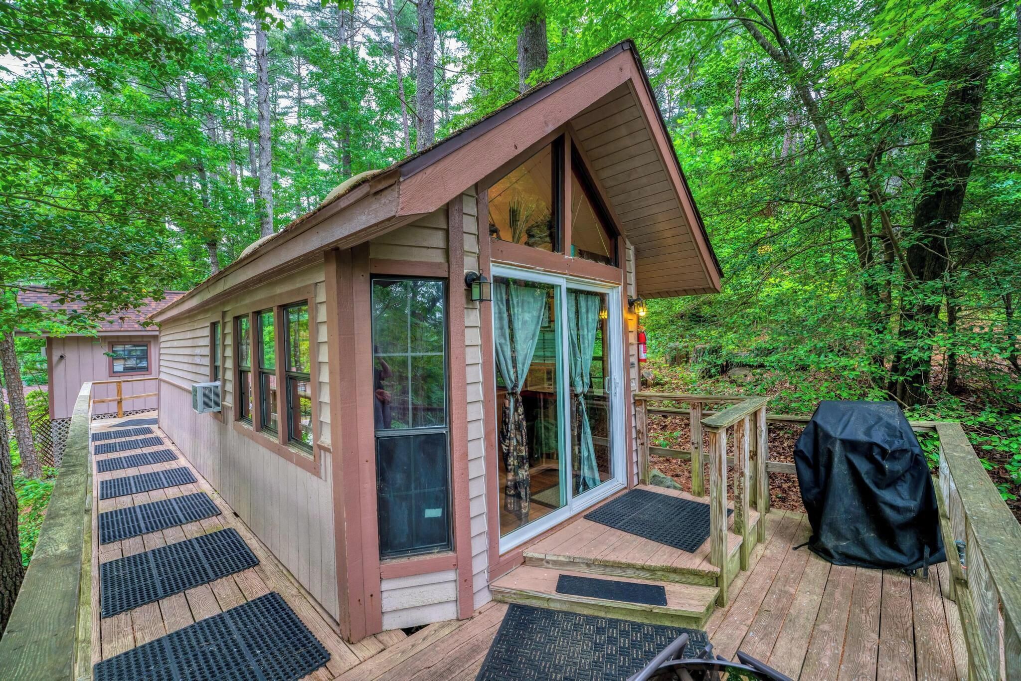 A cabin with a deck, large windows, and a covered outdoor area.