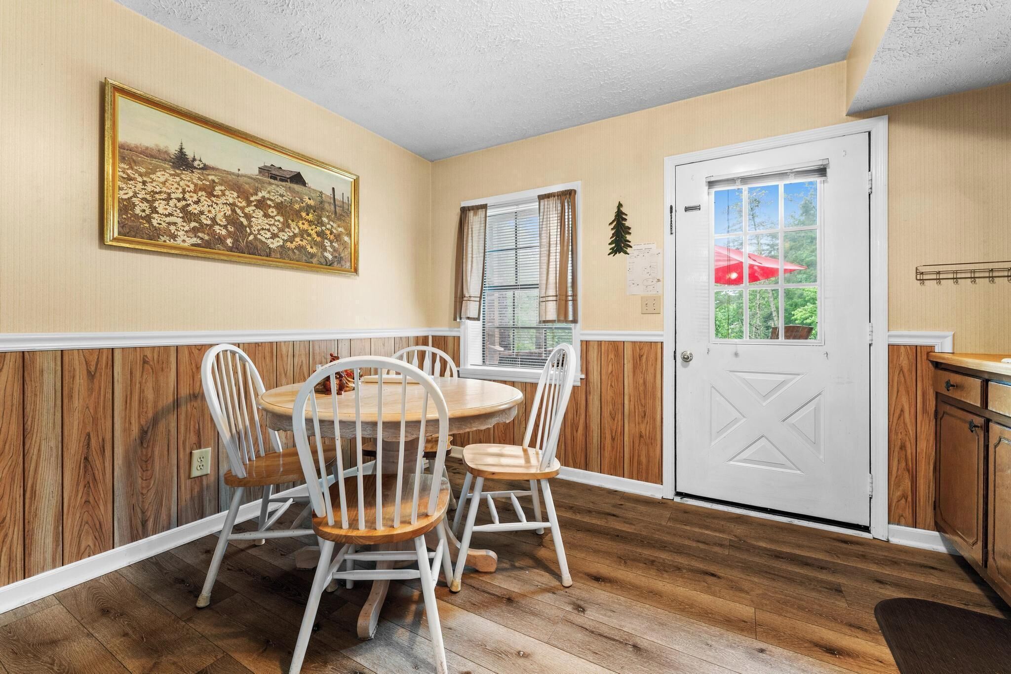 A dining area with a round table and four chairs, a white door, and a window with blinds.