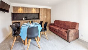 A modern living room with a dining area, featuring a sofa, dining table, chairs, and a kitchen area with wooden cabinets and a flat-screen TV. - Lovely apartment in villa for 6 guests with WIFI, TV, terrace and pets allowed (Le Carquois)