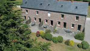 A multi-story brick building with a flat roof, multiple windows, and a patio area with outdoor furniture. - Lovely apartment in villa for 6 guests with WIFI, TV, terrace and pets allowed (Le Carquois)