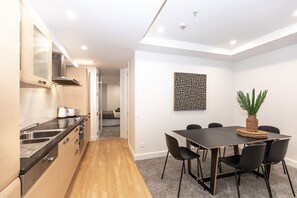 A modern kitchen with wooden cabinets, a built-in oven, and a dining area with a table and chairs. - Chic and Modern P22 Mount Maunganui Apartment (Mount Maunganui)