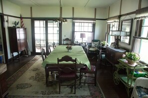 Classic dining room with a long table set for four, flanked by chairs, and featuring a chandelier and large window.