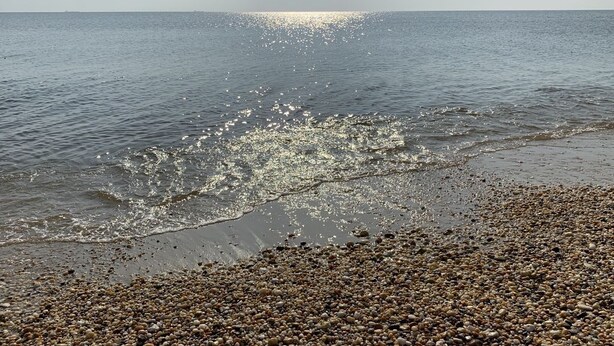Una playa de arena con agua tranquila y el sol reflejándose en la superficie.