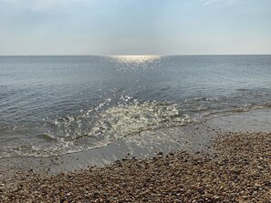 A pebbled beach with calm water and sunlight reflecting off the surface.