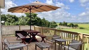 Una terraza de madera con una mesa de picnic, sillas y una sombrilla.