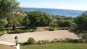 Un jardin avec une zone dallée, des arbres et une vue sur la mer.