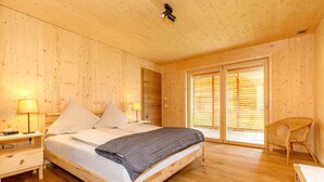 Une chambre à coucher en bois, avec un lit, des tables de chevet, une chaise et une porte-fenêtre coulissante.
