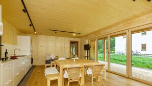 Une cuisine moderne avec des meubles en bois, une table à manger entourée de chaises en osier et de grandes portes-fenêtres coulissantes donnant sur un jardin.