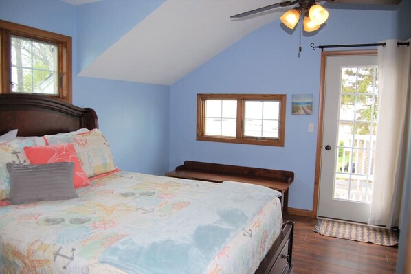 A bedroom with a bed, a window, a door, and a ceiling fan.