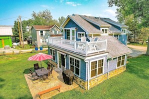 A two-story house with a balcony, a patio with outdoor furniture, and a stone foundation.