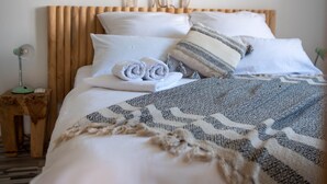 Een keurig opgemaakt bed met opgerolde handdoeken, een gestreept deken en een houten hoofdeinde.