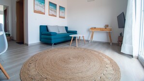 Een moderne woonkamer met een blauwe bank, een rond geweven vloerkleed en een kleine witte tafel.