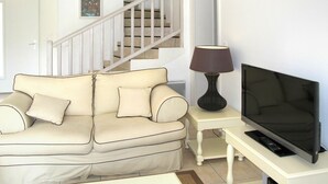 A living room with a beige sofa, a TV on a stand, a lamp, and a staircase in the background. - Beautiful apartment in villa for 8 guests with private pool, TV, terrace and pets allowed (Pont-de-larn)
