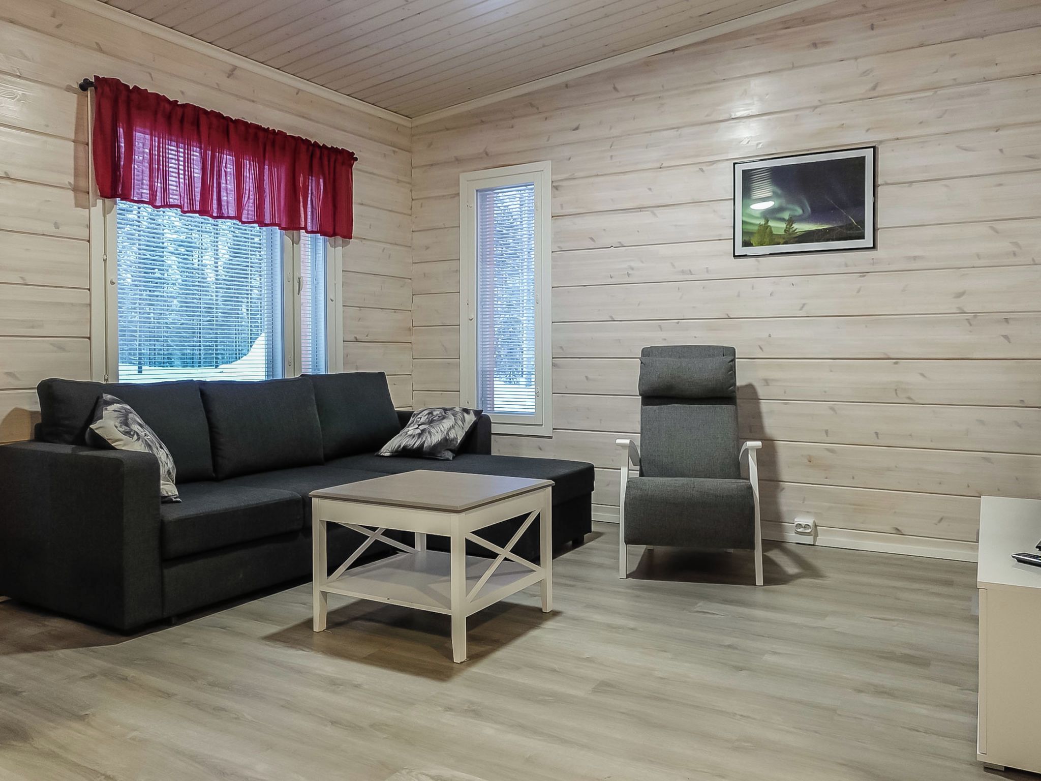 Ett rum med en svart soffa, en grå fåtölj, ett litet vitt bord och ett fönster med persienner.