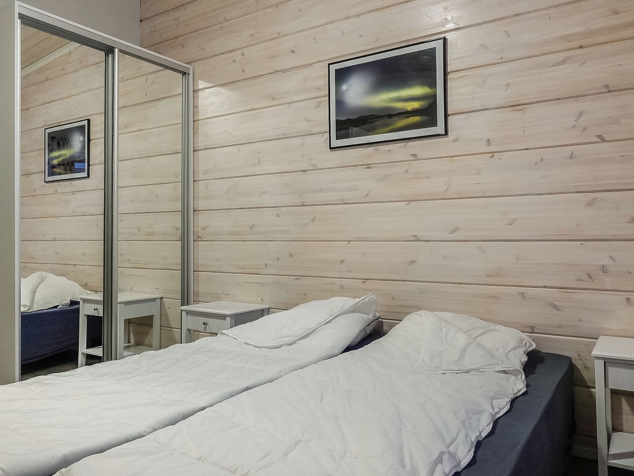 Habitación de hotel con pared de madera, una cama con ropa blanca, dos mesitas de noche y un espejo.