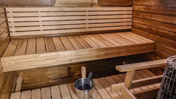A sauna with wooden benches and a metal bucket.