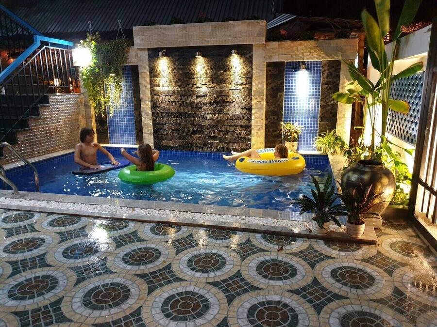 Una piscina interior con suelo de baldosas, una pared con cascada de agua y plantas en macetas.