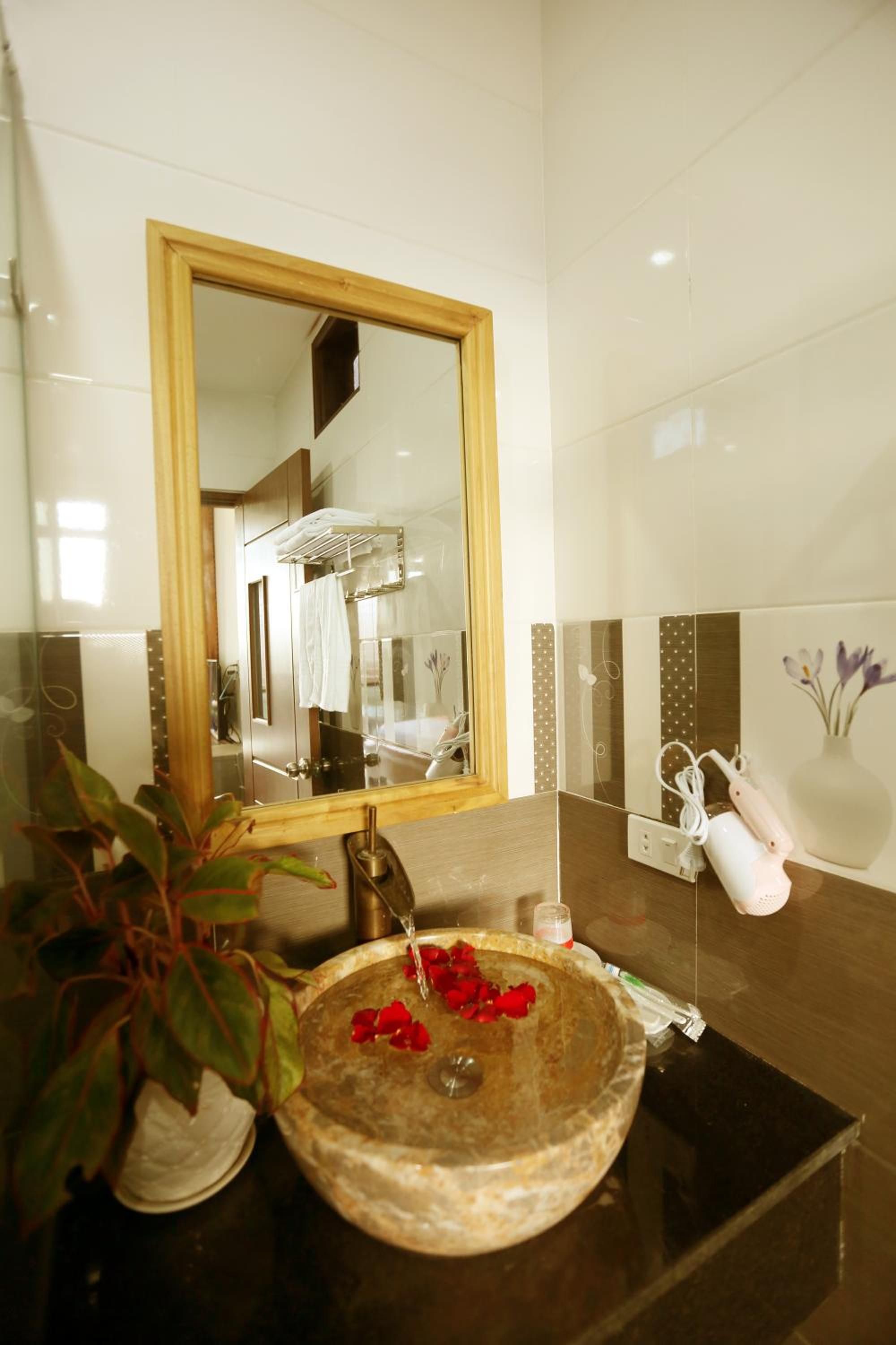 A bathroom with a large mirror, a round sink with rose petals, a towel rack, and a vase with flowers.