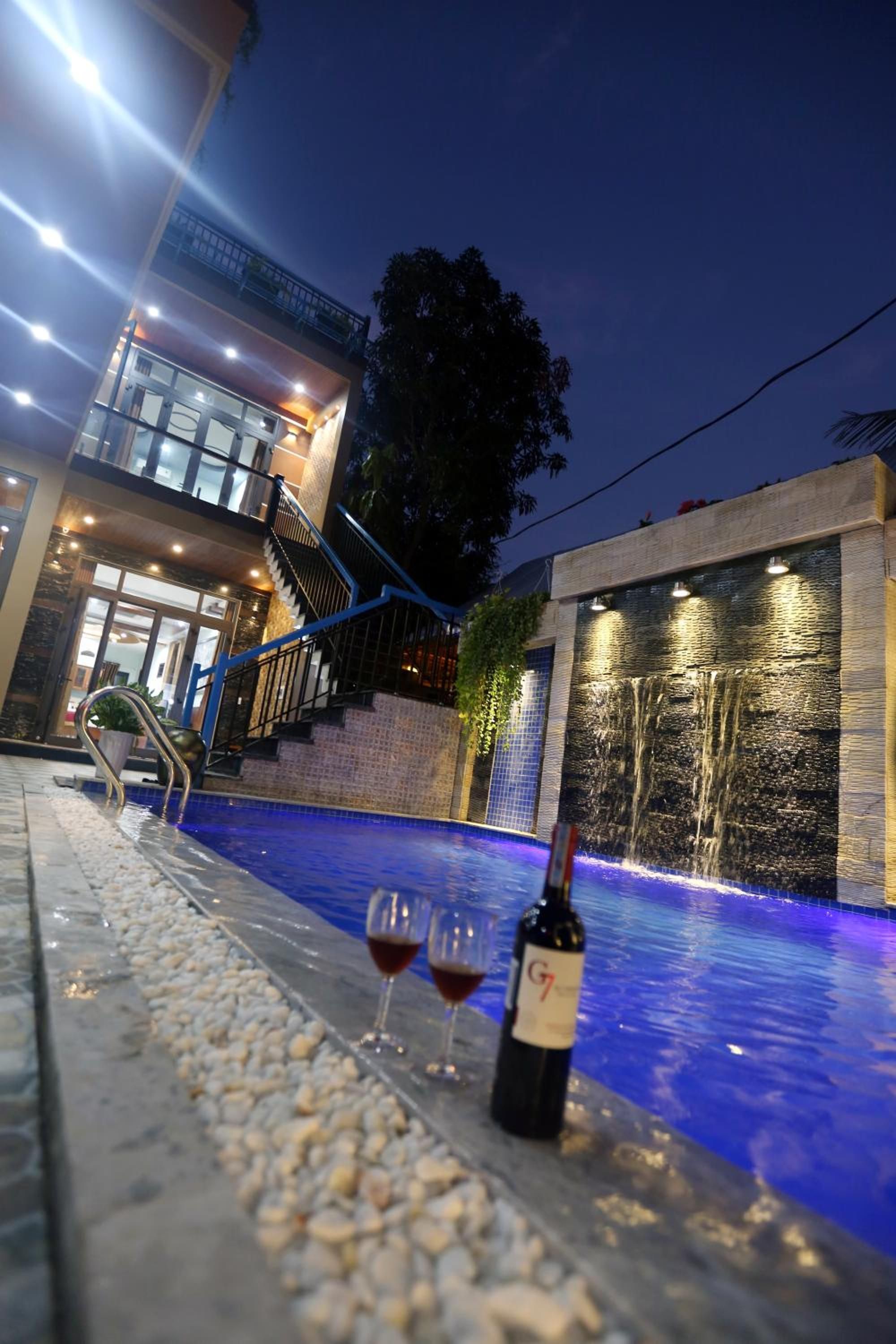 A pool area with a waterfall feature, a staircase, and a bottle of wine on the poolside.