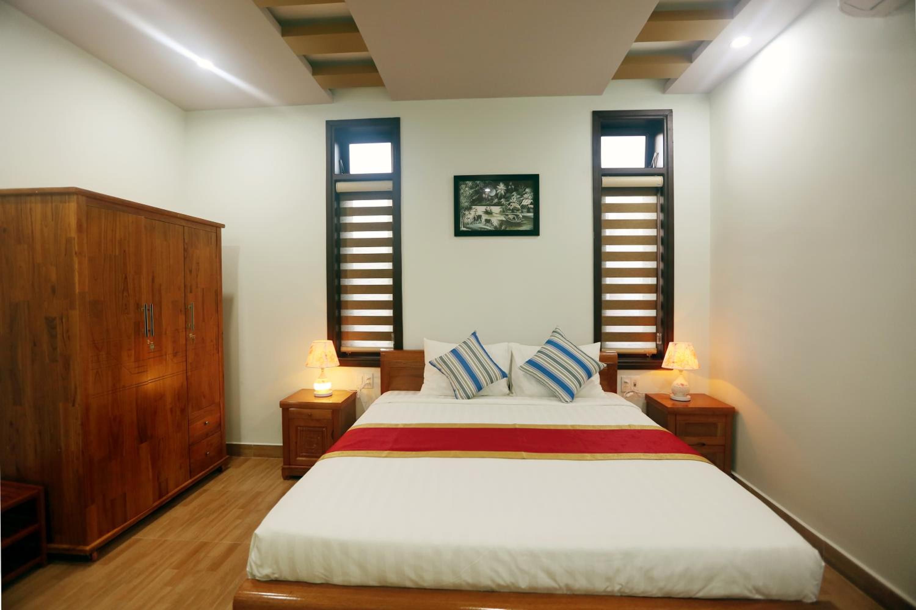 A bedroom with a bed, two nightstands, a wooden wardrobe, and a window with blinds.