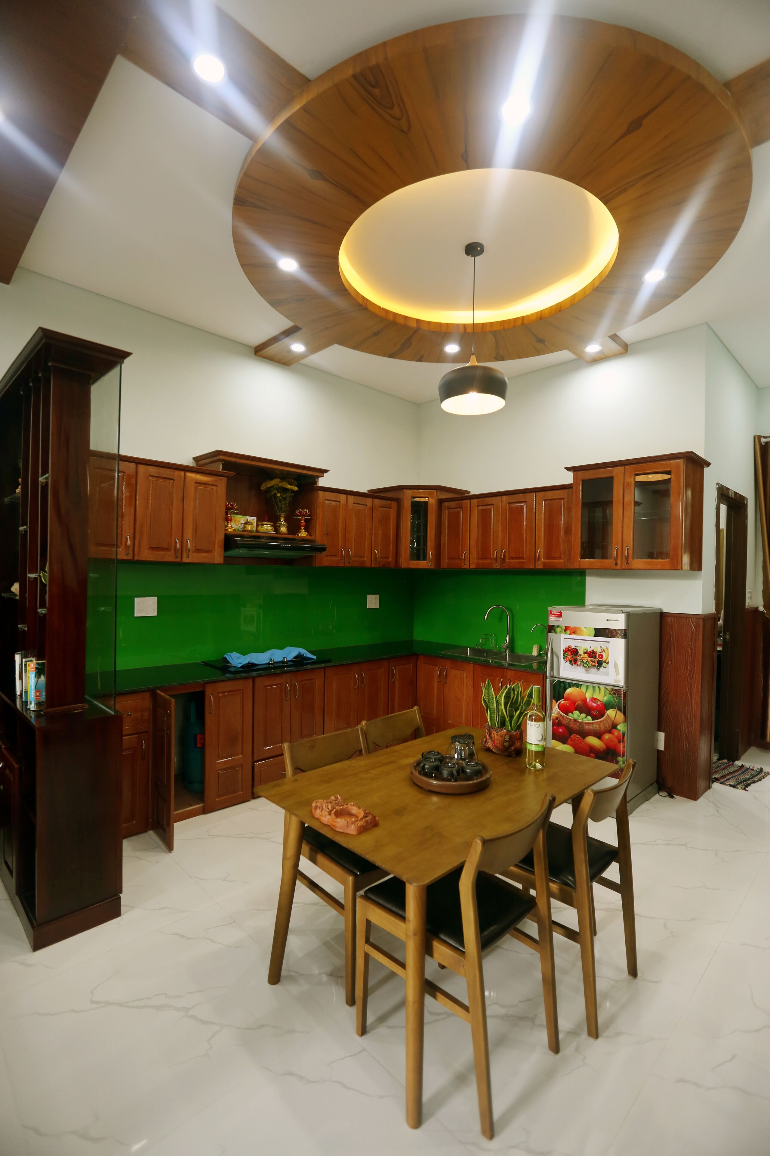 A modern kitchen with wooden cabinets, a green backsplash, and a dining area with a wooden table and chairs.