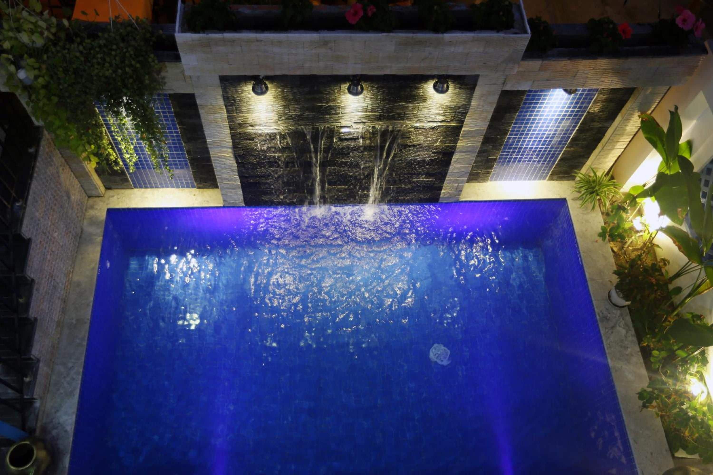 Una piscina en la azotea con una cascada, rodeada de plantas en macetas y un muro de piedra.