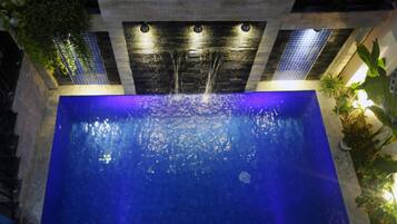Una piscina en la azotea con una cascada, rodeada de plantas en macetas y un muro de piedra.