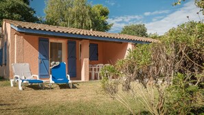 Une petite maison avec un toit en tuiles, une porte d’entrée et une chaise bleue dans la cour.