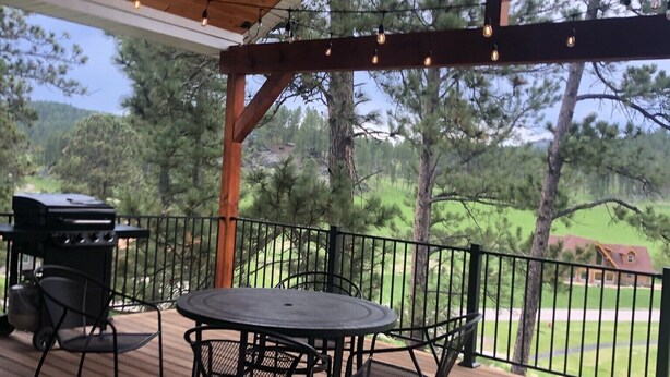 A covered outdoor deck with a table and chairs, string lights, and a grill. - Spacious home with Hot Tub, bikes, fire pit, pool table and more!! (Hill City)