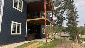 A two-story house with a covered patio area, a hot tub, and a small deck. - Spacious home with Hot Tub, bikes, fire pit, pool table and more!! (Hill City)