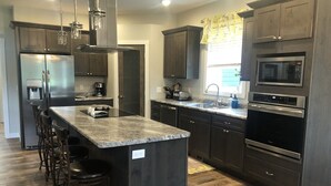 A modern kitchen with dark cabinets, stainless steel appliances, and a central island with bar stools. - Spacious home with Hot Tub, bikes, fire pit, pool table and more!! (Hill City)