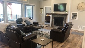 A living room with leather sofas, a coffee table, a fireplace, a TV, and a clock on the wall. - Spacious home with Hot Tub, bikes, fire pit, pool table and more!! (Hill City)