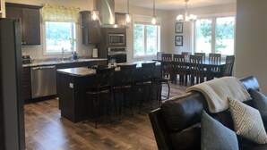 A modern kitchen with a central island, bar stools, and a dining area with a large table and chairs. - Spacious home with Hot Tub, bikes, fire pit, pool table and more!! (Hill City)