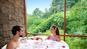 Una pareja en un jacuzzi con pétalos de rosa, rodeada de exuberante follaje.