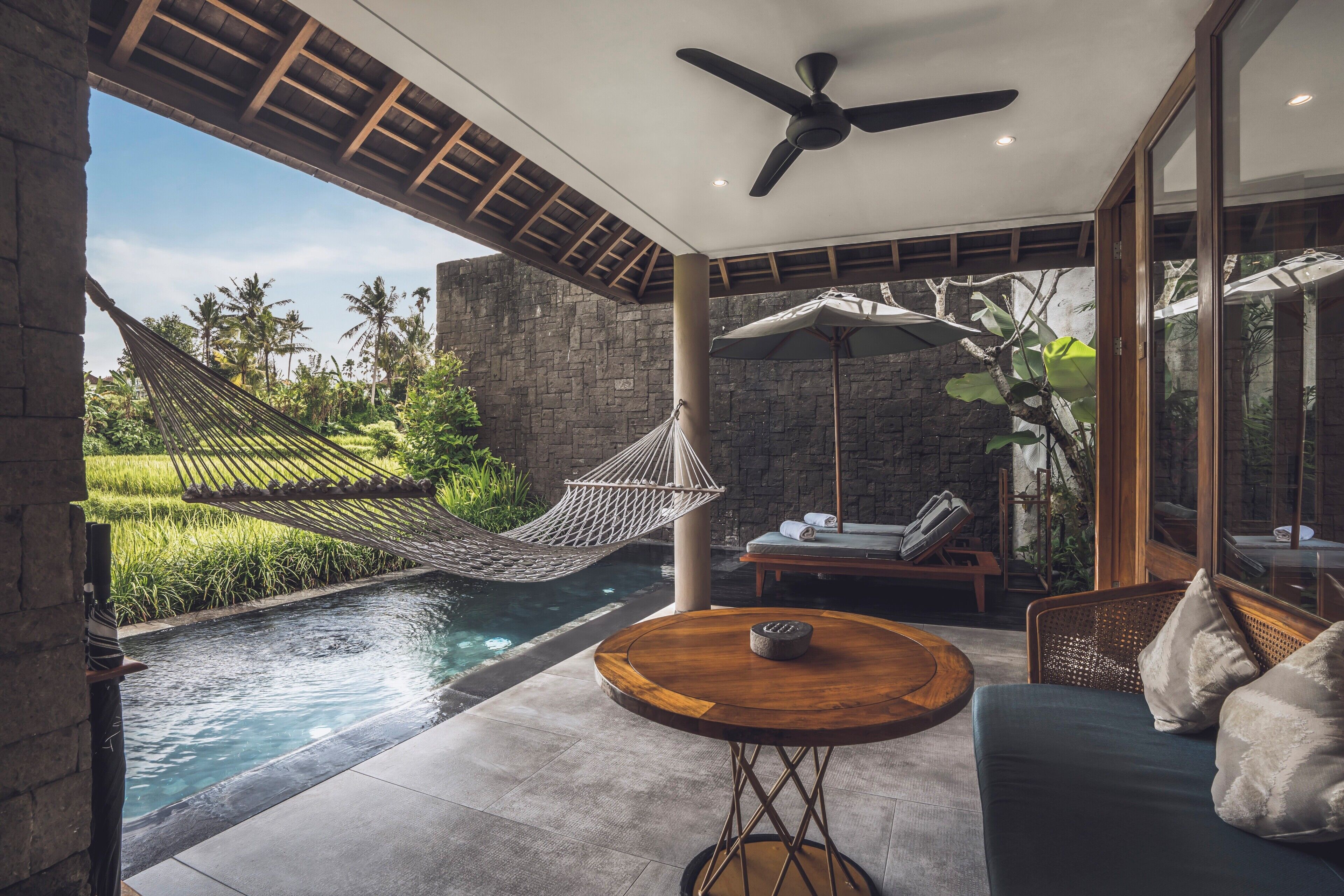 A modern outdoor seating area with a pool, a hammock, and a ceiling fan.