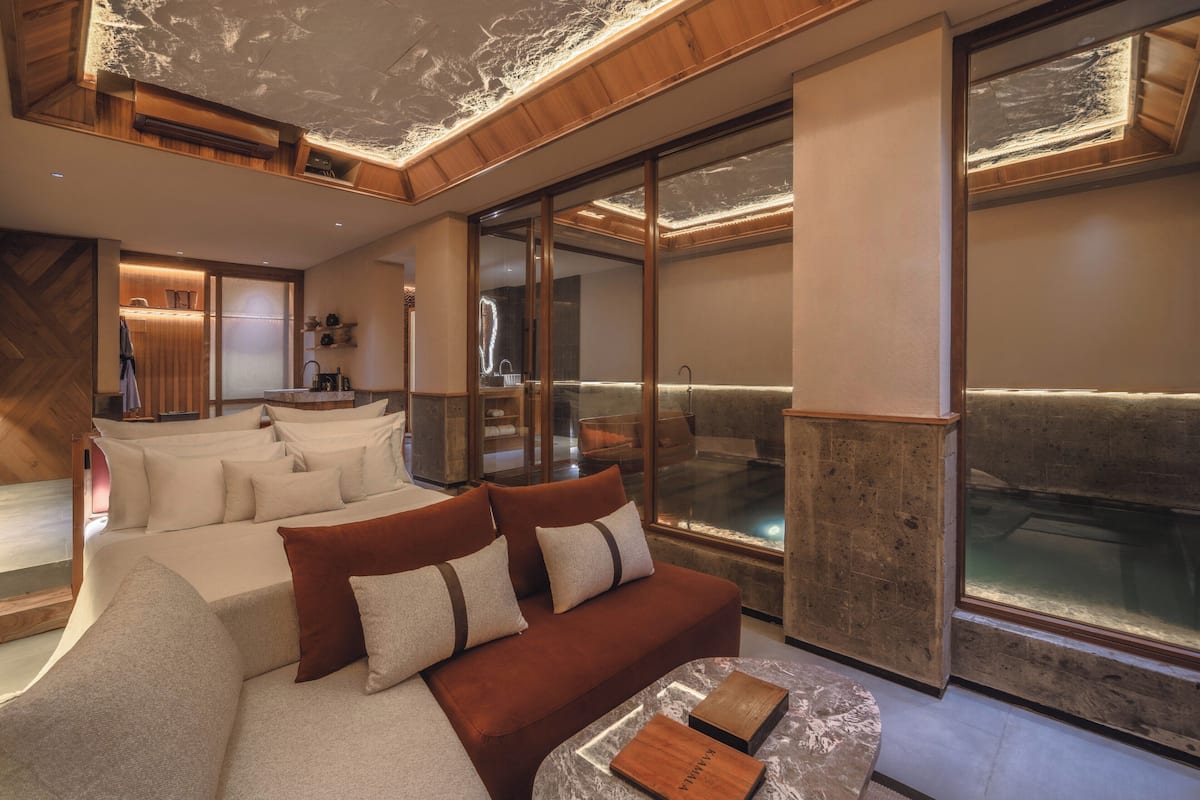 A modern hotel room with a large bed, a sofa, a small table, and a large window.